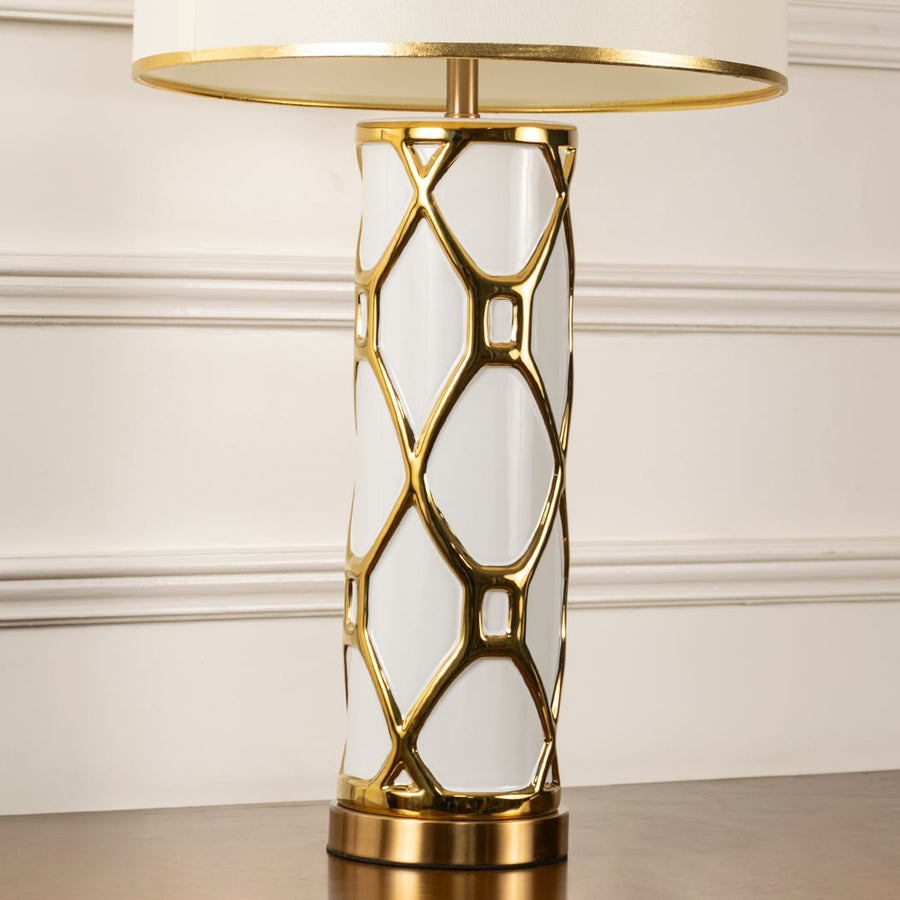 Closeup of gold lattice frame table lamp with white shade on carved console table with light off for luxurious decorative décor.