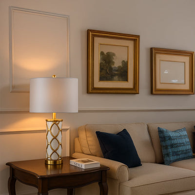 White and gold ceramic table lamp with fabric shade placed on wooden console for elegant living room decor styling.