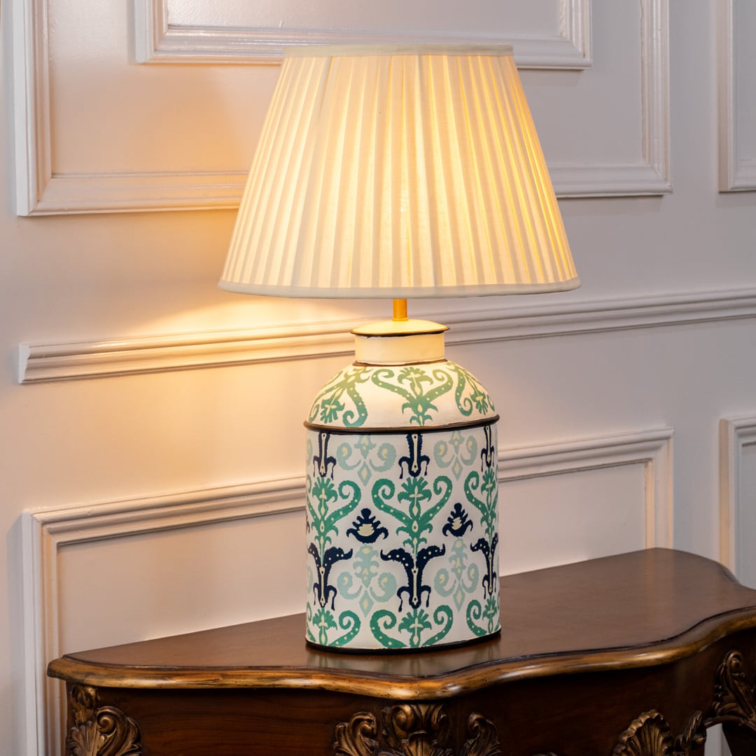 Table lamp on white background showcasing a mint green ceramic base with traditional floral patterns finished with a pleated fabric lampshade.