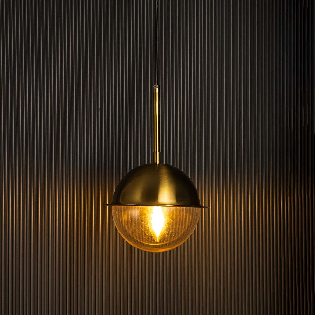 Brass dome pendant light glowing warmly with clear glass globe on black background perfect for dining and living areas.