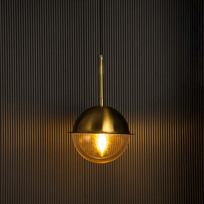 Brass dome pendant light glowing warmly with clear glass globe on black background perfect for dining and living areas.