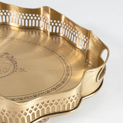 A closeup view of the gold serving tray showing its intricate engraved center scalloped border and fine metal texture with detailed craftsmanship visible.