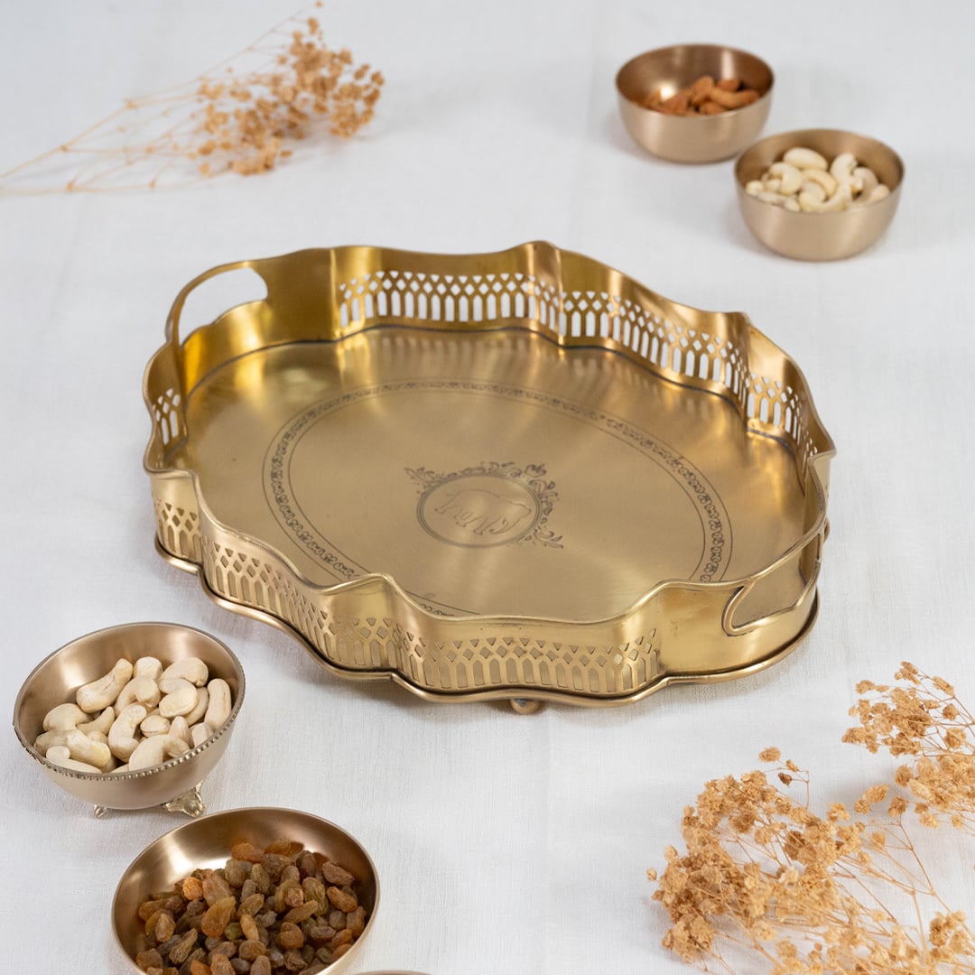 Gold brass serving tray with wavy rim cutwork border and engraved base displayed on plain white background.