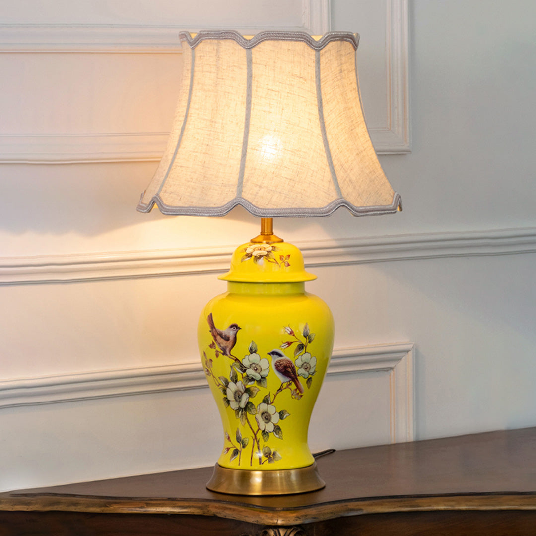 Yellow floral ceramic table lamp with scalloped fabric shade creating warm traditional ambient lighting on a wooden console table.