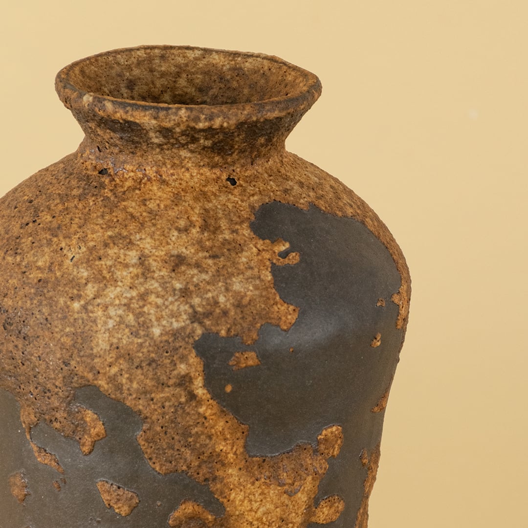Closeup image of rustic ceramic decorative vase with textured brown and black finish shown with light off on a dark black background highlighting the handcrafted surface details.