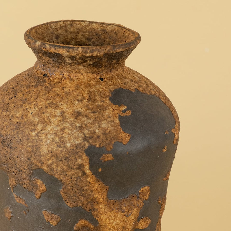 Closeup image of rustic ceramic decorative vase with textured brown and black finish shown with light off on a dark black background highlighting the handcrafted surface details.
