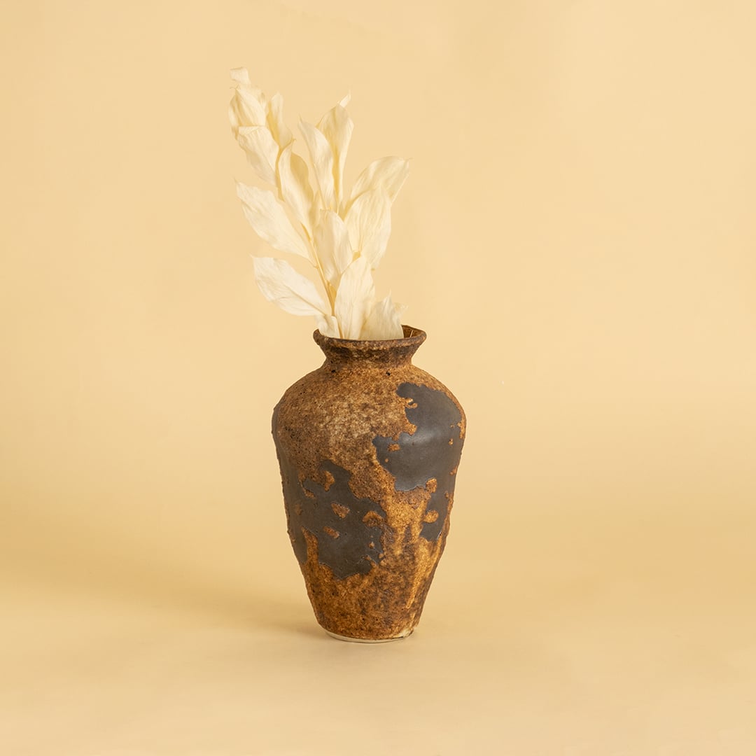 Tall rustic brown ceramic vase with textured finish styled on wooden table adding earthy charm to home interior decor