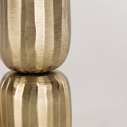 Close view of gold metal vase showing vertical fluted texture and round base with polished sculptural finish