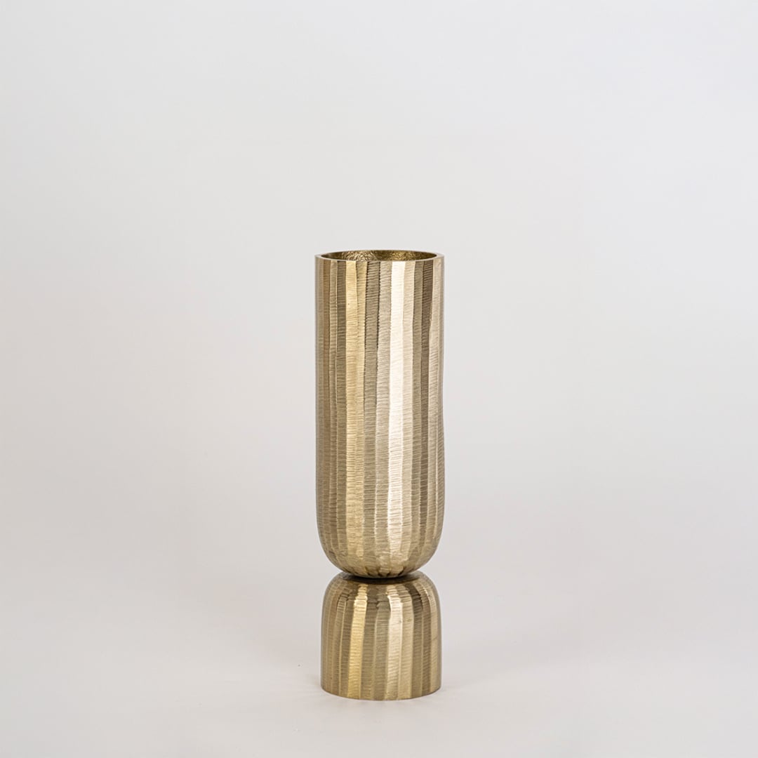 Gold metal vase with vertical ribbed surface and round base displayed clearly against plain white background wall