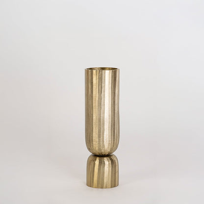 Gold metal vase with vertical ribbed surface and round base displayed clearly against plain white background wall