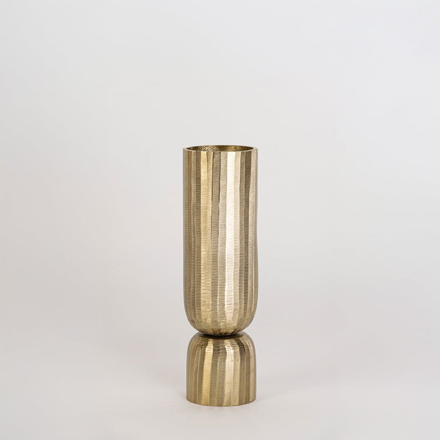 Gold metal vase with vertical ribbed surface and round base displayed clearly against plain white background wall