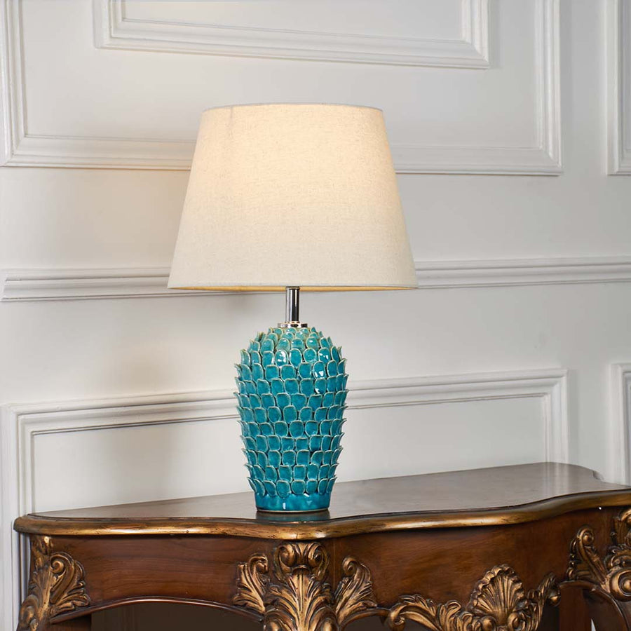 Turquoise textured glass table lamp with fabric shade displayed on a carved wooden console table creating elegant ambient lighting.