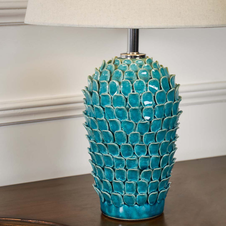 Closeup of turquoise ceramic table lamp with bold textured scale pattern and cream shade showcasing detailed craftsmanship and modern style.