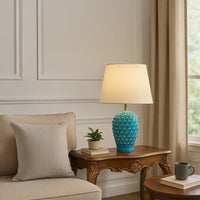 Turquoise ceramic textured table lamp with a cream shade placed on a carved wooden side table adding a bright modern accent to living room decor.