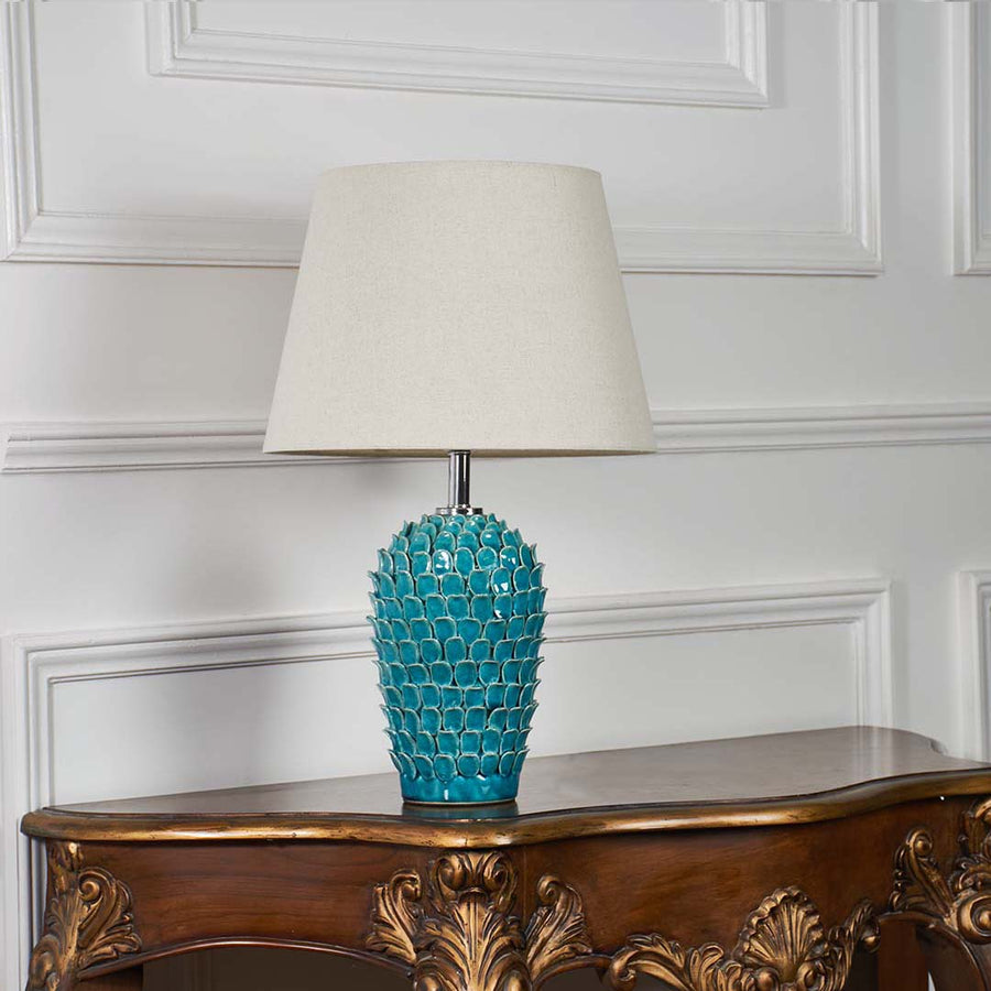 Modern turquoise ceramic lamp turned off with scale patterned texture and cream shade shown on a white background for elegant decor presentation.
