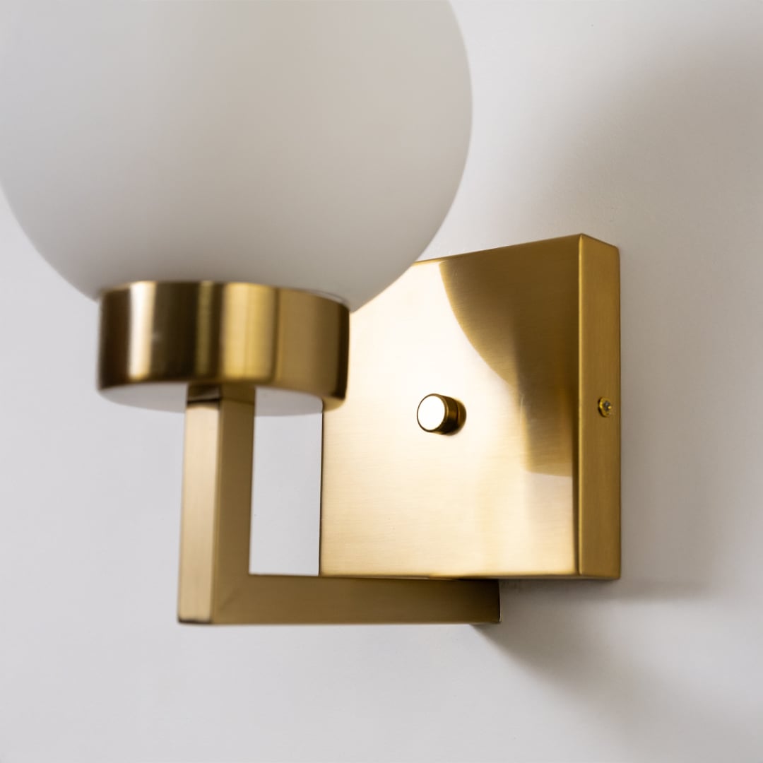 Closeup of gold metal wall light with frosted glass globe shade showing premium detailing for elegant contemporary indoor lighting.