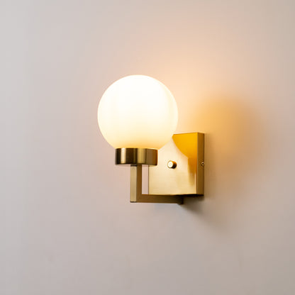 Modern wall light in gold metal finish with globe glass shade for bedroom or living decor lighting white background.