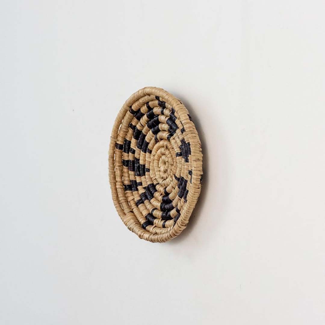 Handwoven wicker wall plate side view in beige and black natural fiber showing artisan weave texture and product thickness.