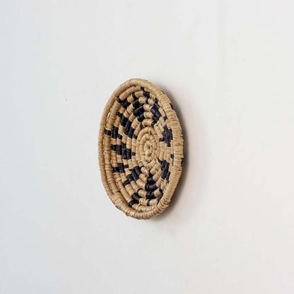 Handwoven wicker wall plate side view in beige and black natural fiber showing artisan weave texture and product thickness.