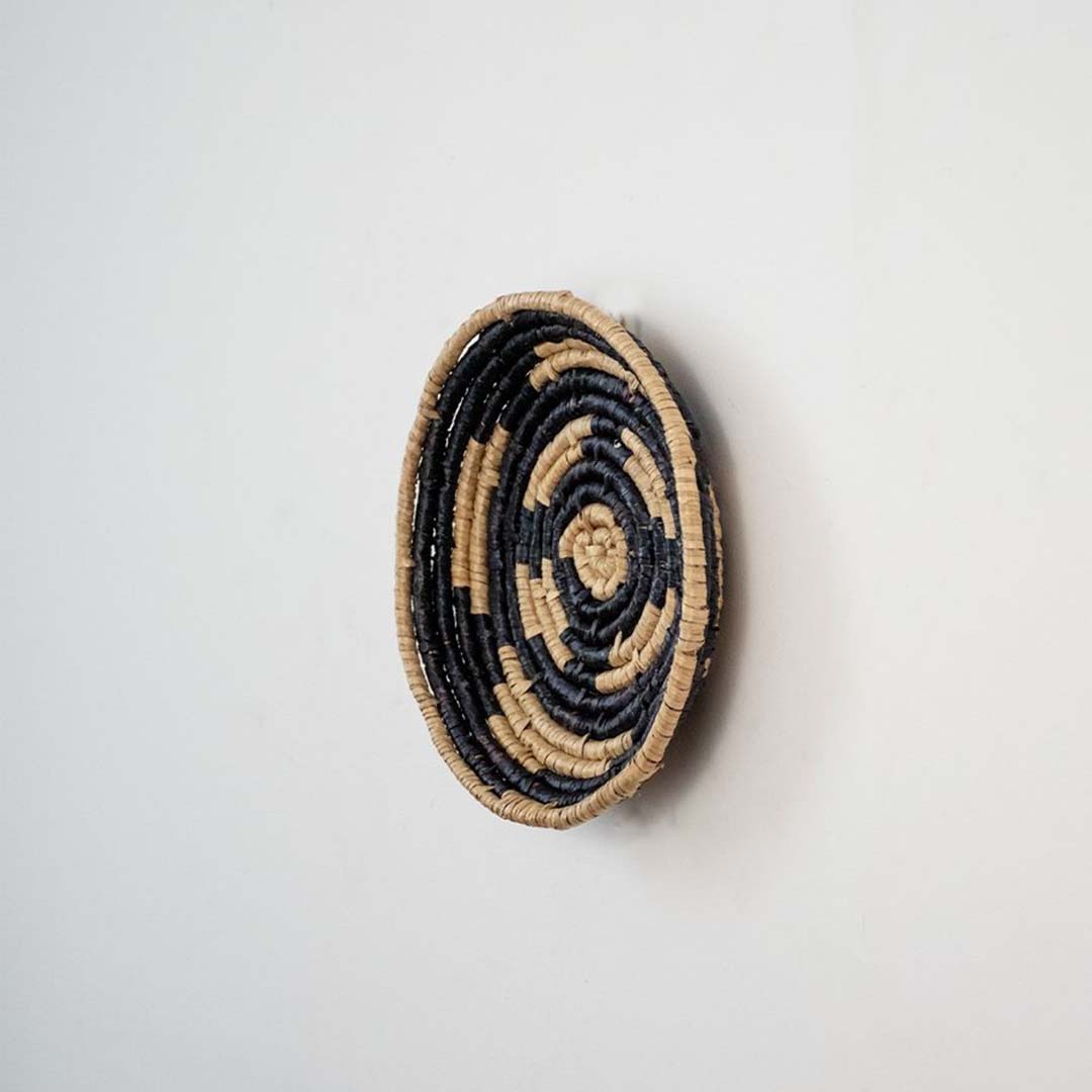 Handwoven wicker wall decor plate side view in beige and black natural fiber showing spiral weave texture and plate depth.