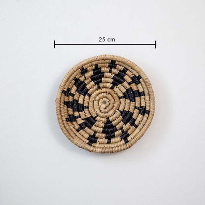 Handwoven wicker wall decor plate 25 cm round in beige and black natural fiber light off white background with size shown.