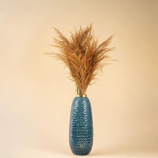 Tall blue zigzag ceramic vase with gold rim styled with dried pampas grass against a soft beige background for a modern decor look.