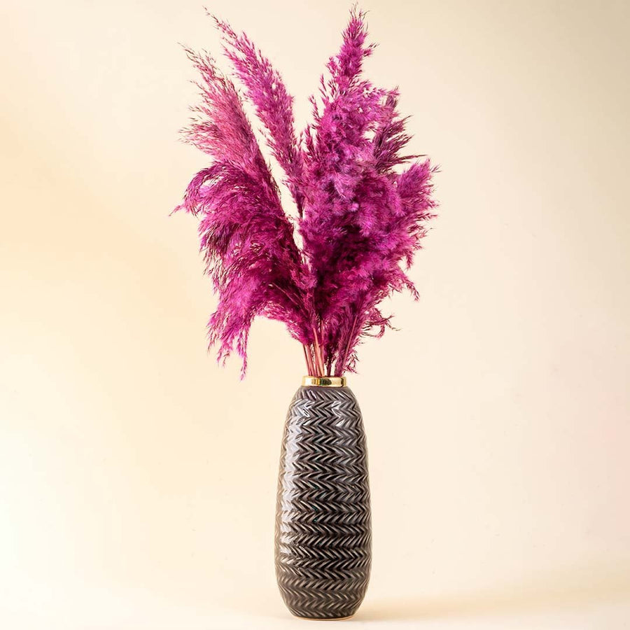 Tall grey zigzag ceramic vase with gold rim styled with vibrant purple pampas grass against a soft beige background.