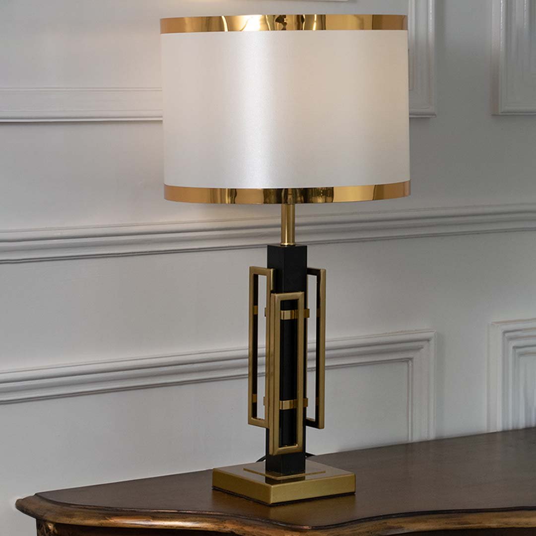 Gold metal geometric table lamp with fabric drum shade displayed on a console table creating luxury ambient lighting.