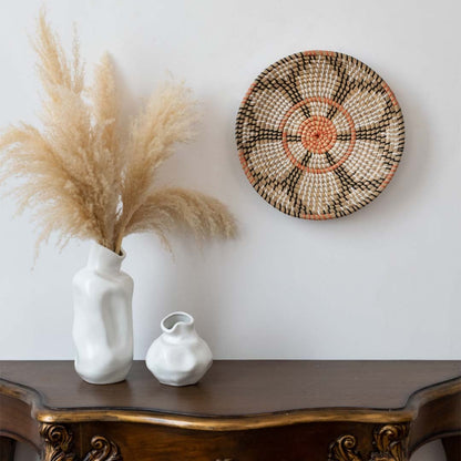 Handwoven wall basket decor in natural orange and black fiber styled above console table with vase for boho wall.