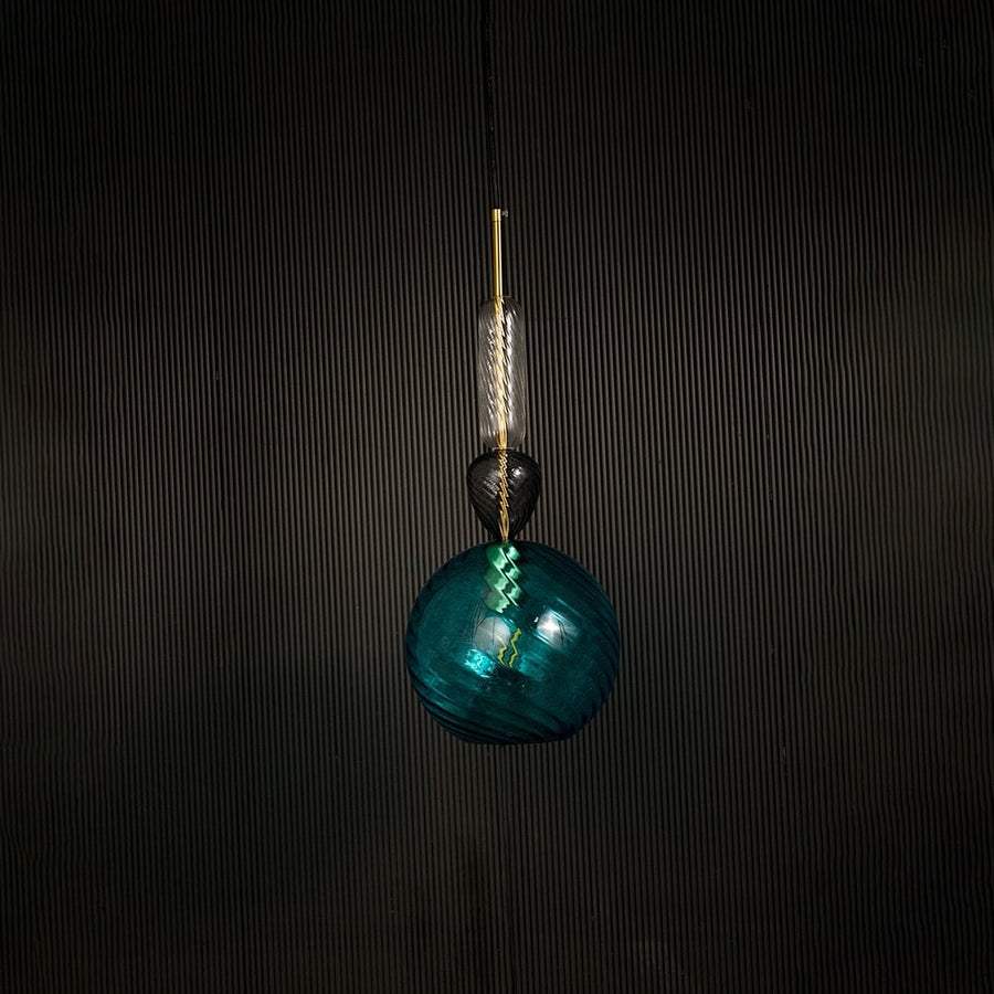 Artistic blue glass pendant light with golden detailing displayed on dark background with light off for elegant modern lighting style.