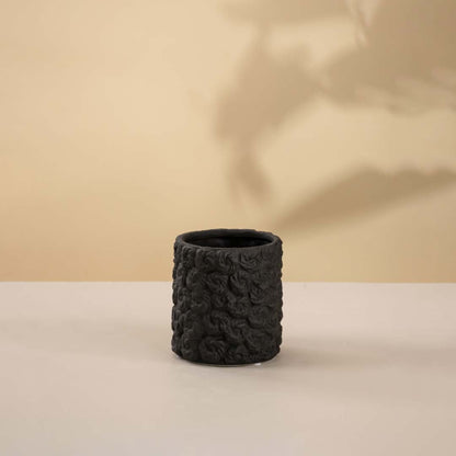 Modern handcrafted black ceramic vase with circular form and detailed surface texture against white backdrop.