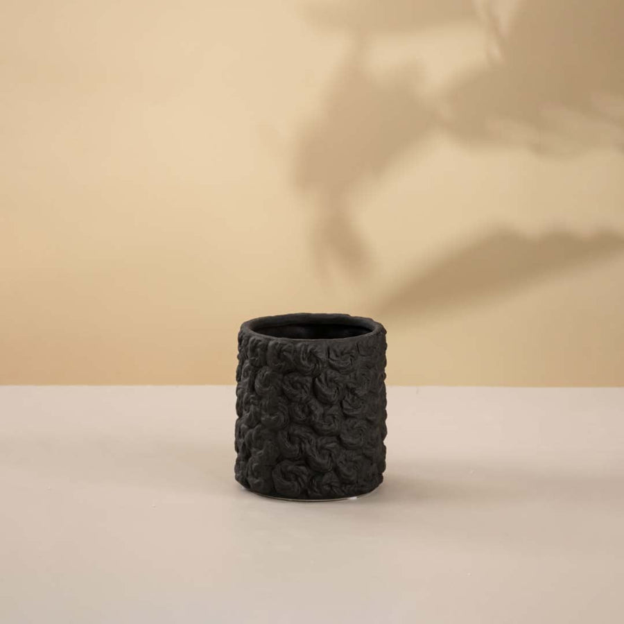 Modern handcrafted black ceramic vase with circular form and detailed surface texture against white backdrop.