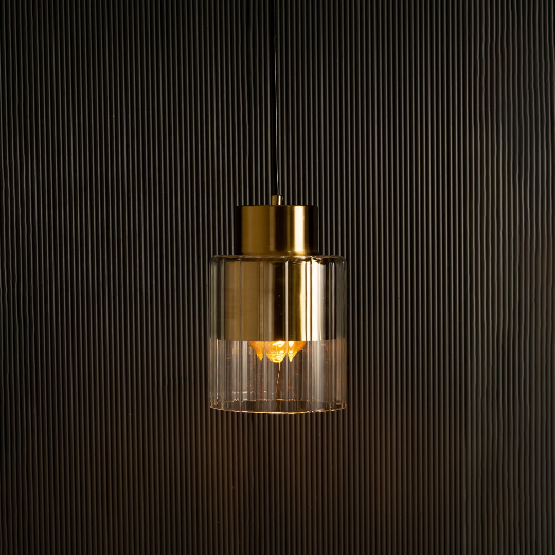 Gold metal and glass pendant illuminated against a dark backdrop highlighting its soft light and reflective metallic surface.