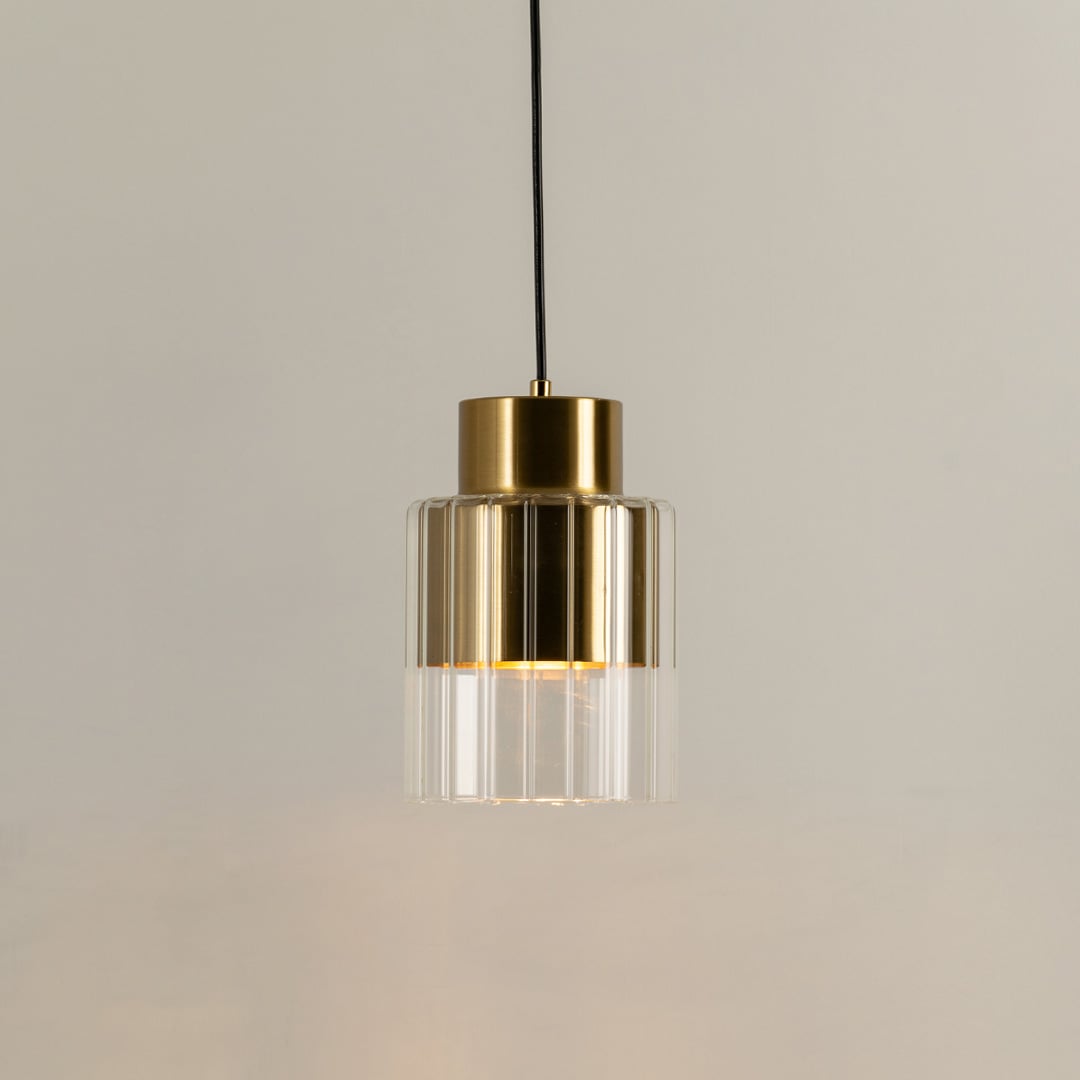 Gold metal pendant light with clear glass diffuser illuminated to highlight premium modern decorative lighting.