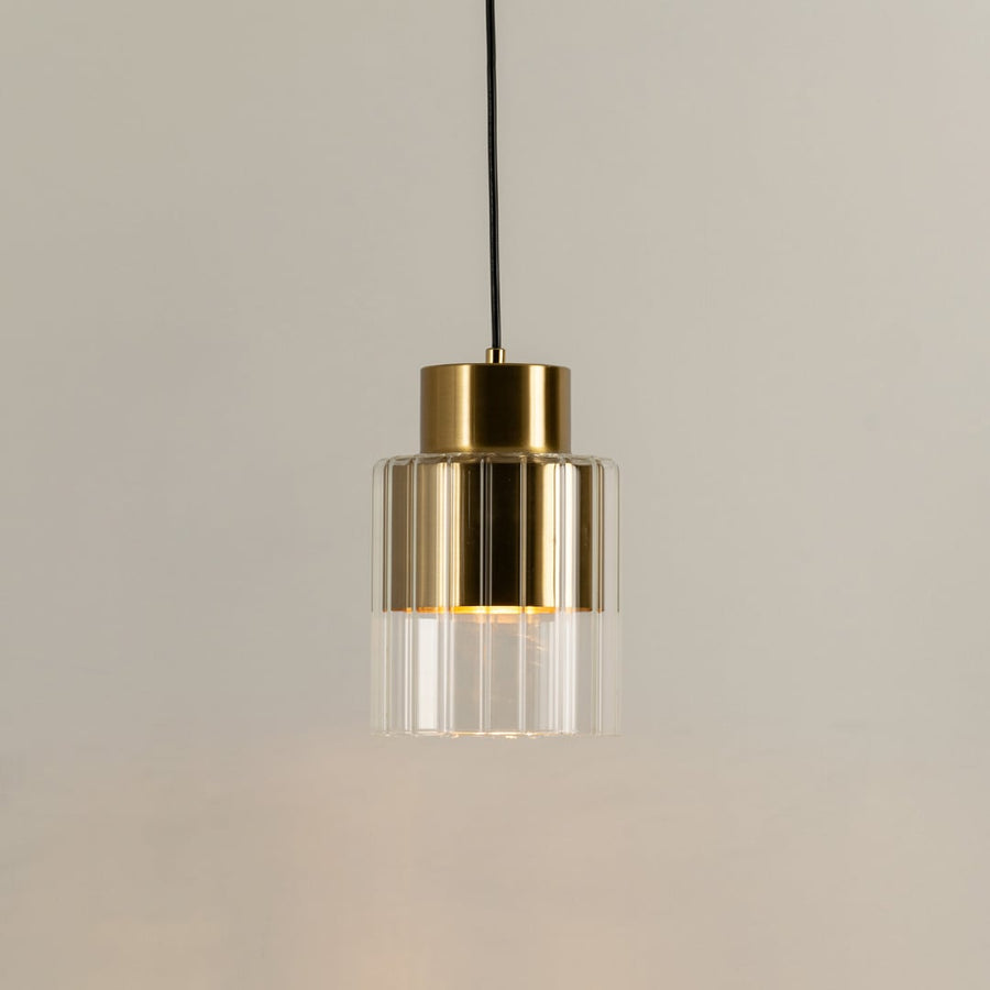 Gold metal pendant light with clear glass diffuser illuminated to highlight premium modern decorative lighting.