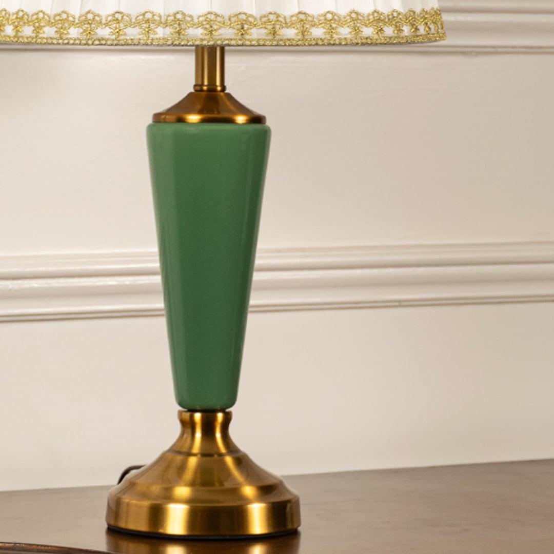 Table lamp closeup showing green metal base and pleated white shade with gold detailing for elegant interior accents.