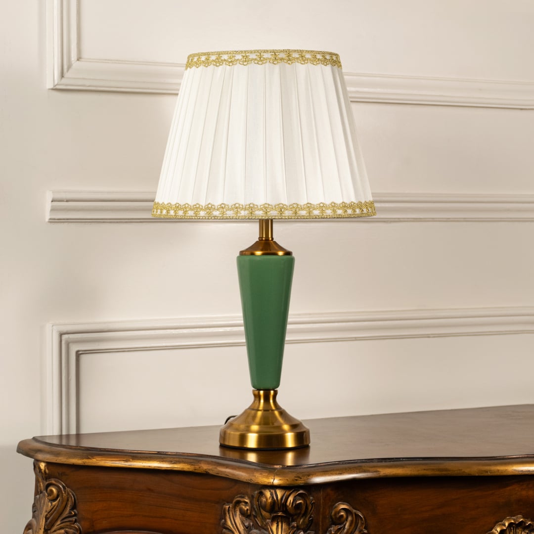 Table lamp with green metal base and pleated white shade displayed on a soft white background for clean product viewing.