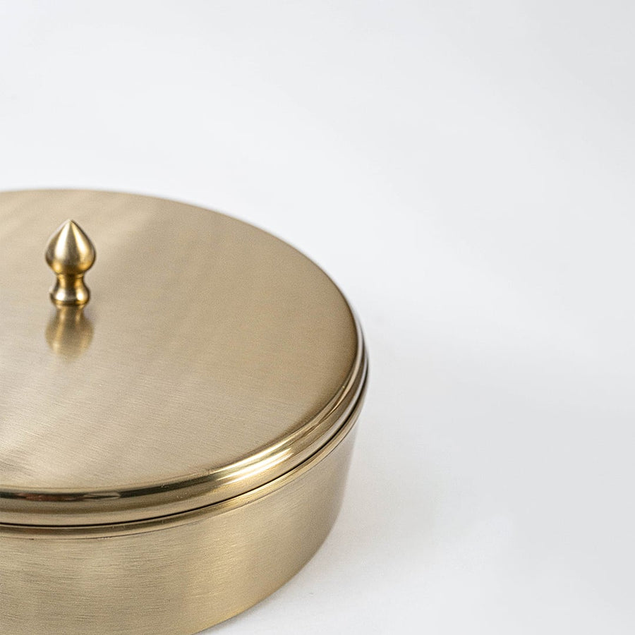 Brass masala box filled with colorful Indian spices arranged in compartments placed on rustic kitchen counter setup.