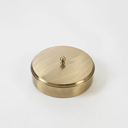 Round brass spice box packed in a black branded gift box with lid partially open shown on clean white background.