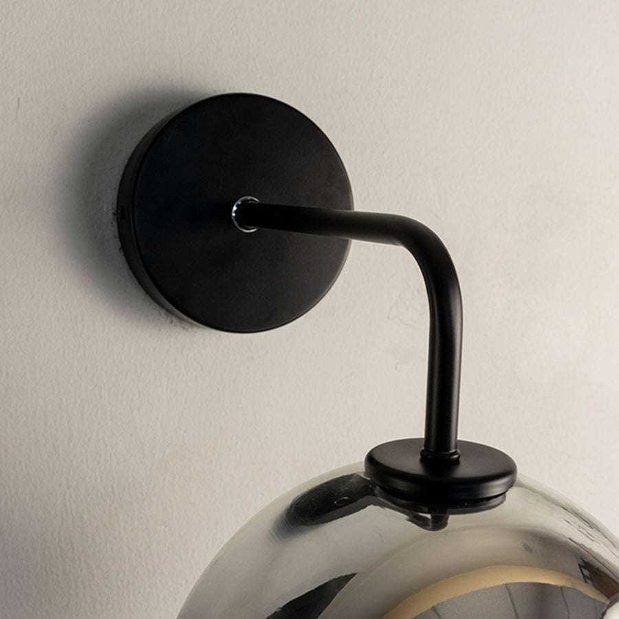 Modern black metal wall light with smoked glass globe and sleek curved arm for stylish interiors.