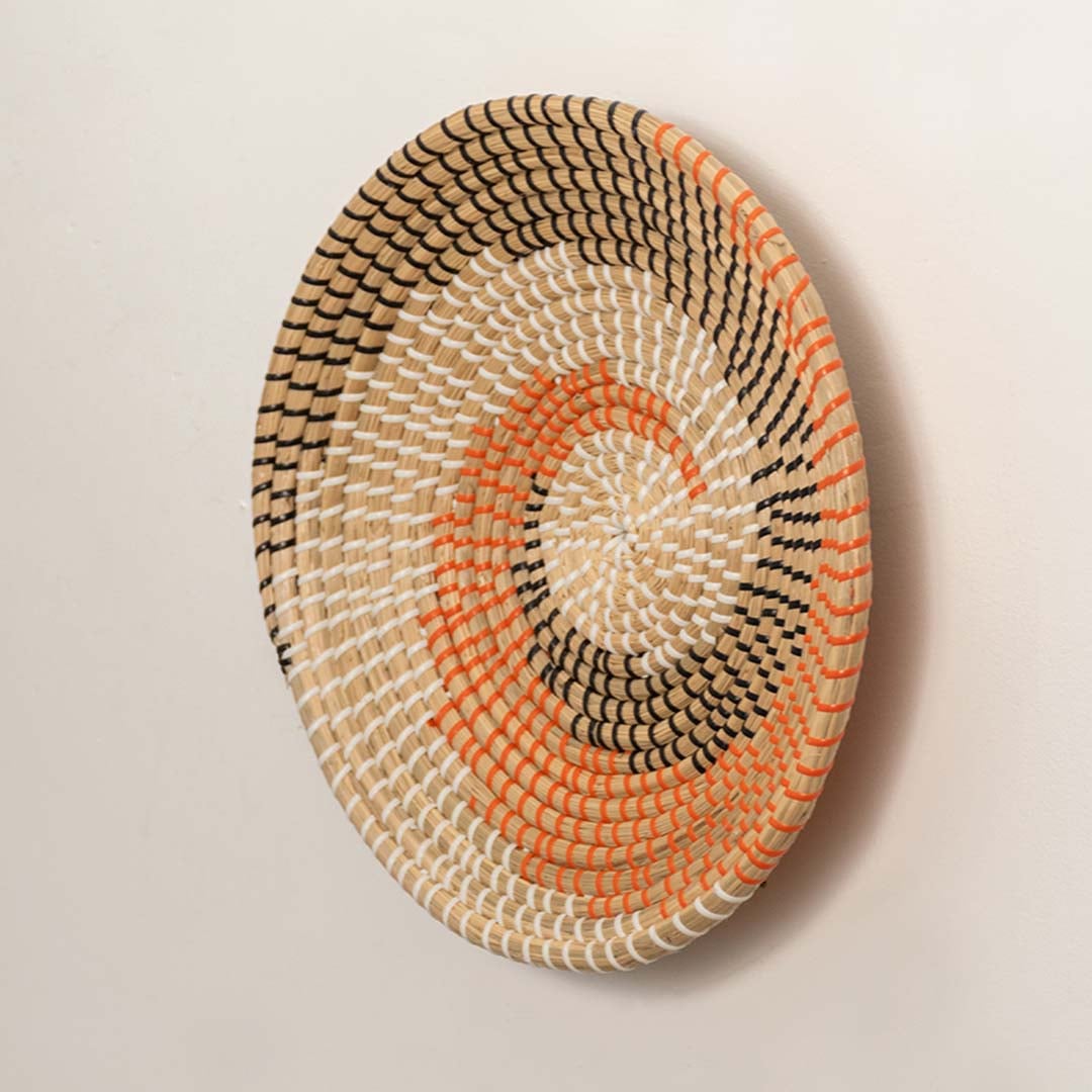 Side angle view of handwoven spiral wall plate in natural beige with orange and black accents.