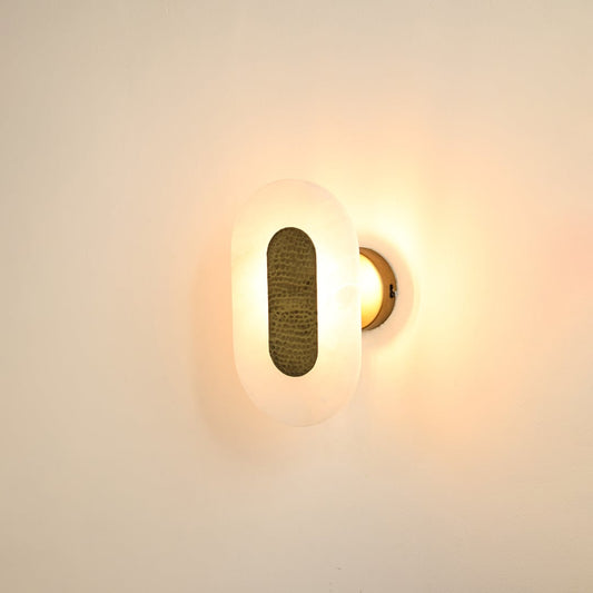 Oval alabaster wall sconce illuminated on white background featuring warm brass texture and soft diffused glow ideal for luxury home lighting.