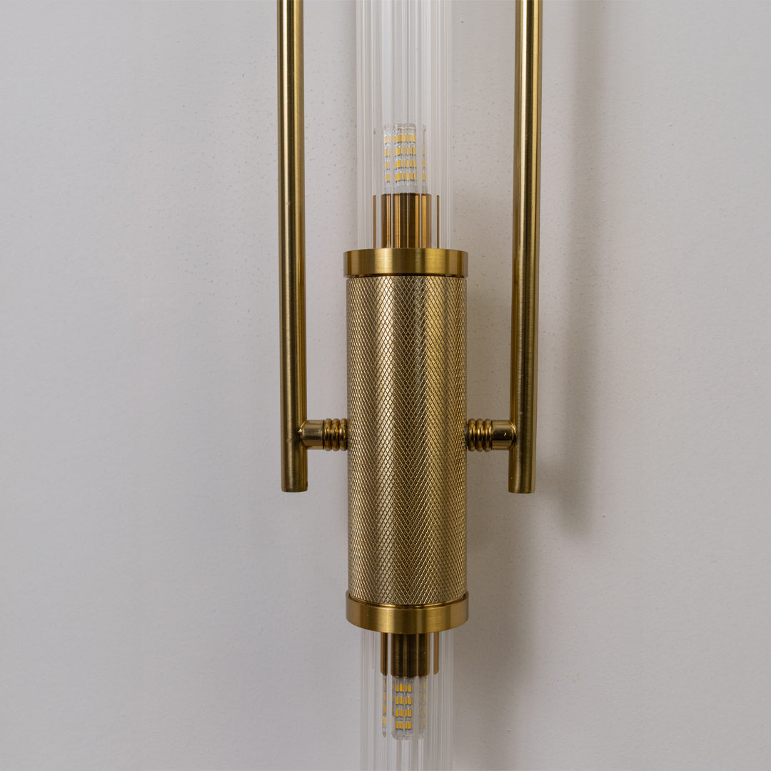 Closeup wall light in gold metal finish with cylindrical detail for bedroom or living decor lighting white background.