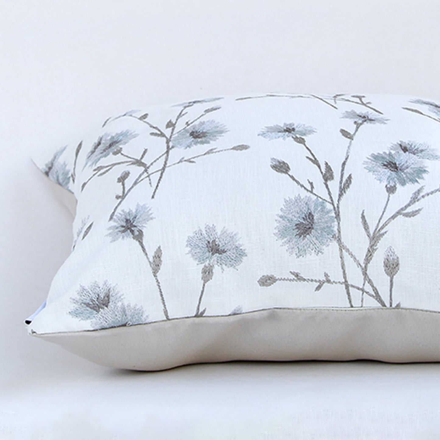 Closeup of the cushion showing detailed blue floral embroidery on a soft white fabric surface.
