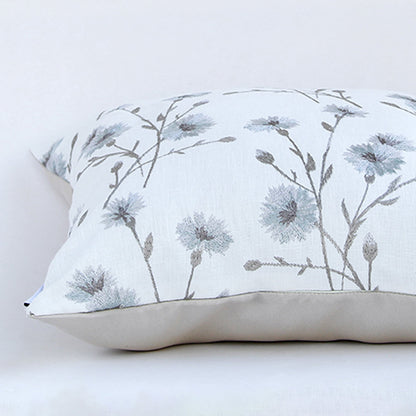 Closeup of the cushion showing detailed blue floral embroidery on a soft white fabric surface.