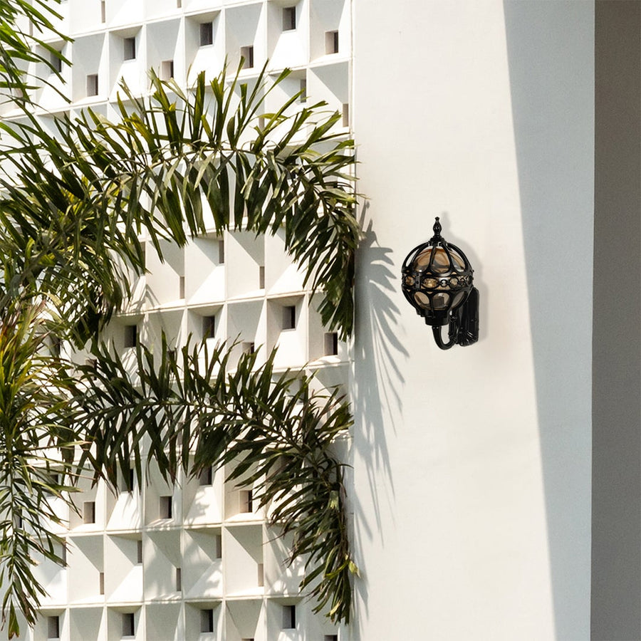 Black metal outdoor wall lantern with globe design mounted on a white exterior wall providing elegant daytime decor for modern patios and entryways.