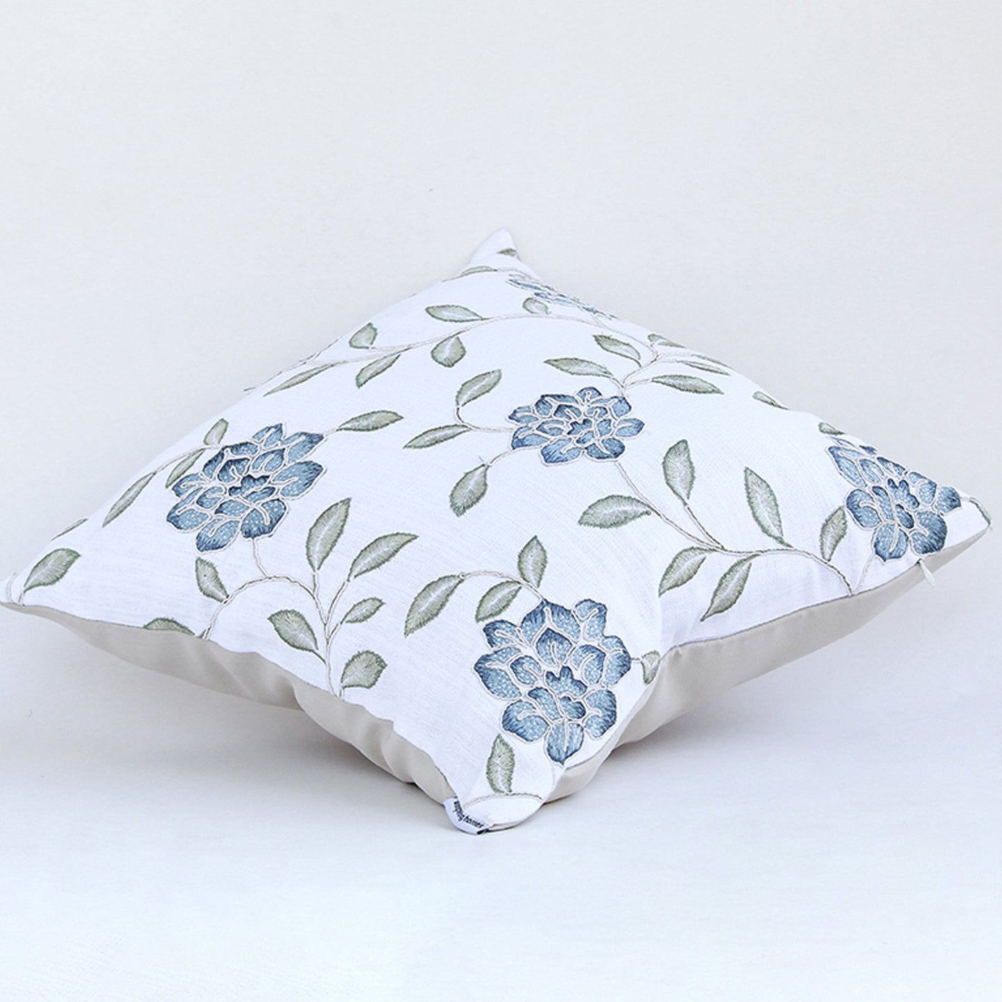 Blue floral embroidered cotton cushion shown on a clean white background showcasing intricate stitched motifs and plush decorative fabric texture.