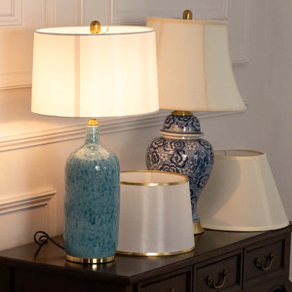 Ceramic table lamps light on with blue ceramic bases and white shades placed on a wooden console creating a soft warm glow in decor setup.