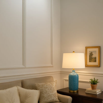 Modern blue ceramic table lamp with gold metal base and white fabric shade adds elegance and a refreshing coastal charm to interiors.