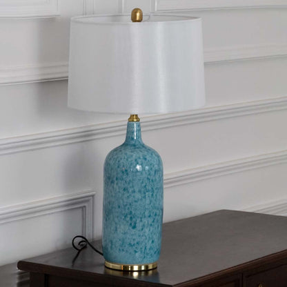 Unlit blue ceramic table lamp with gold base and white shade highlights handcrafted elegance as a decorative statement piece.